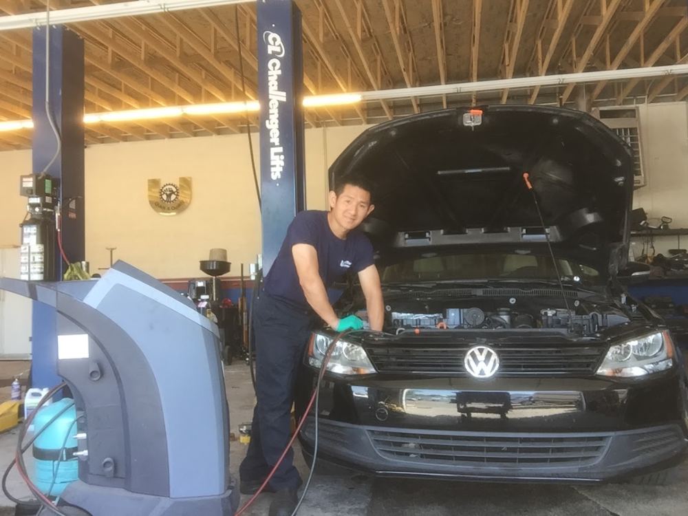 A Unitech mechanic smiling next to a Volkswagen with an A/C service machine hooked up